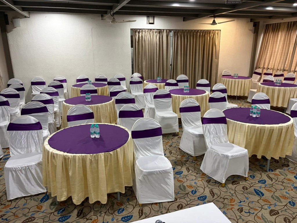 Banquet hall seating with white chair covers and purple sashes at Hotel Chaitali